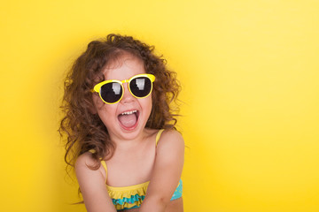 Little girl in a bathing suit and sunglasses on a yellow background