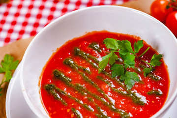 Tomato cold gazpacho soup with pesto sauce in white bowl. Close up