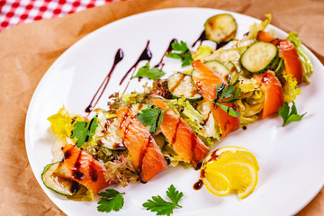 Salad with salmon, cucumber and mixed greens on white plate. Close up