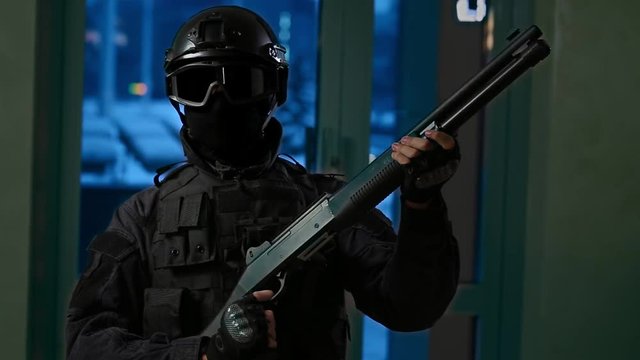 A commando in black uniform with a shotgun in his hands looks into the camera, reloads the weapon.