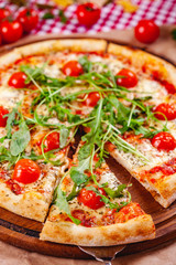 Italian Pizza with tomatoes, mozzarella cheese and arugula on wooden cutting board. Close up