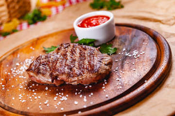 Grilled beef steak with tomato sauce on wooden cutting board. Close up