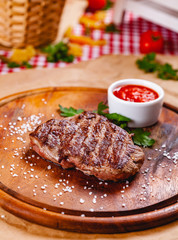 Grilled beef steak with tomato sauce on wooden cutting board. Close up
