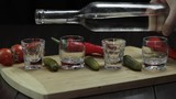 Pour vodka into shot glasses placed on a wooden board