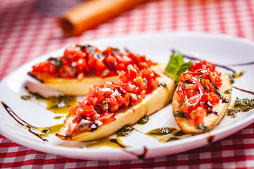 Traditional Italian bruschetta with cherry tomatoes, pesto sauce and balsamic vinegar on white plate. Close up