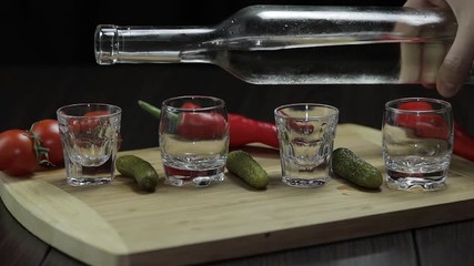 Pour vodka into shot glasses placed on a wooden board