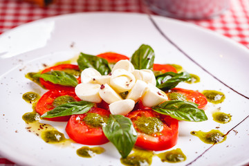 Traditional Italian caprese salad with sliced tomatoes, mozzarella cheese, basil and pesto sauce on white plate. Close up