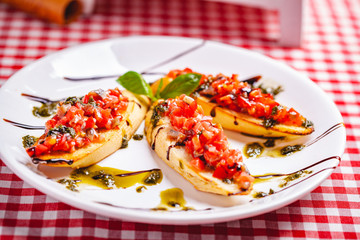 Traditional Italian bruschetta with cherry tomatoes, pesto sauce and balsamic vinegar on white plate. Close up
