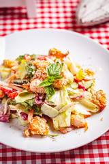 Salad with salmon, vegetables and mixed greens on white plate. Close up