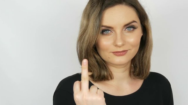 Beautiful sexy bitch girl with flowing hair and blue eyes gently looks into the camera and then shows a fuck sign on a white background. Female aggression.