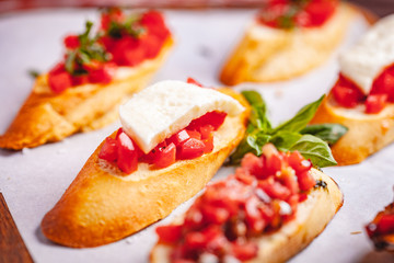 Traditional Italian bruschetta with cherry tomatoes, basil and mozzarella cheese on wooden cutting board. Close up