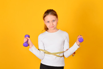 Young and athletic girl does physical exercises with dumbbells, on a yellow background