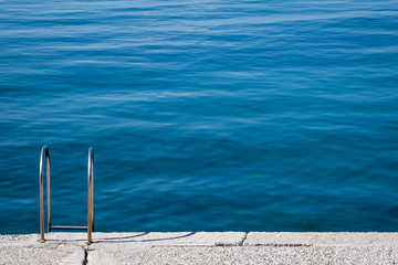 Steel ladder on pier with turquoise adriatic ocean in Triest