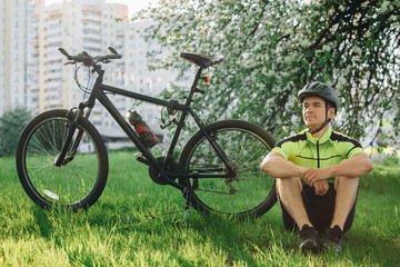 Professional cyclist in helmet and spotswear sitting with mountain bicycle near blooming tree....