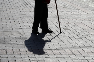 Silhouette of old person walking with a cane, long shadow on pavement. Concept for disability, old age, limping or blind man, diseases of the spine, elderly people