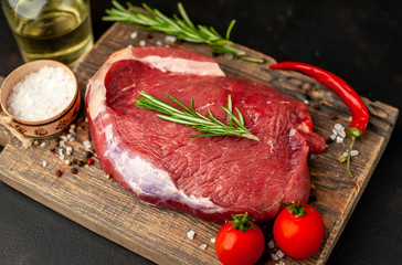 Raw fresh steak with herbs, on a cutting board, stone background, top view