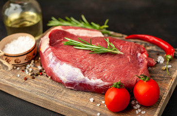 Raw fresh steak with herbs, on a cutting board, stone background, top view