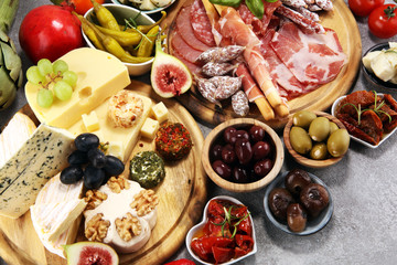 Italian antipasti wine snacks set. Cheese variety, Mediterranean olives, crudo, Prosciutto di Parma, salami and wine in glasses over grunge background.