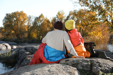 Couple of campers in sleeping bags sitting on rock