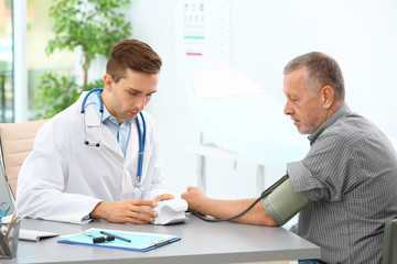 Doctor measuring blood pressure of mature patient in hospital