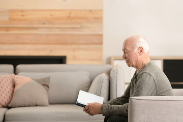 Elderly man reading book in living room. Space for text