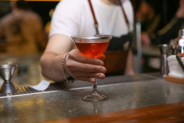 Bartender with glass of tasty cocktail at counter in nightclub, closeup