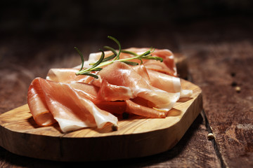 Italian prosciutto crudo or jamon with rosemary. Raw ham on rustic background