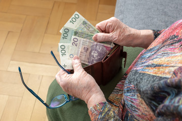 Hands of an elderly pensioner holding leather wallet with polish currency money. Concept of financial security in old age.