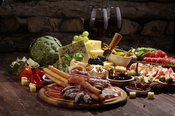 Italian antipasti wine snacks set. Cheese variety, Mediterranean olives, crudo, Prosciutto di Parma, salami and wine in glasses over grunge background.