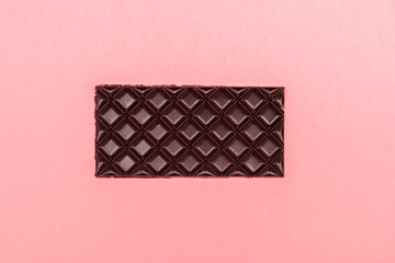 Brown chocolate bar on pink background. Copy space