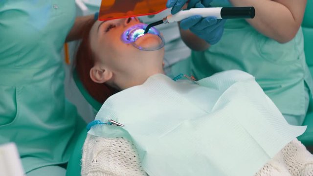 Female dentist with an assistant carry out teeth whitening procedure.