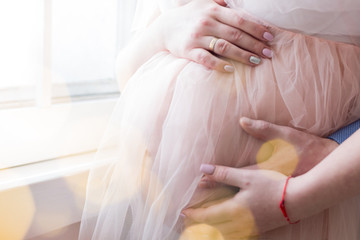 Fototapeta premium pregnant girl in peach-colored negligee. the hands of men and women in the abdomen. 