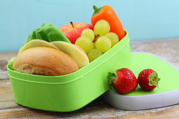 Healthy school lunch box containing cheese sandwich,  crunchy yellow pepper and fresh fruit: apple, strawberries and grapes