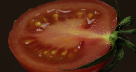 Rotate of the halves of fresh ripe cut tomato on a dark background
