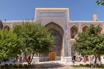 Obraz premium The Ulugh Beg madrasah view from the yard. In the courtyard of the Madrasah with trees. Inside the Madrasah on Registan square in Samarkand. Ancient Madrasah in Uzbekistan. Sunny summer day.