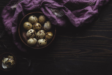 Organic quail eggs in wooden bowl on dark wooden background. With copy space.