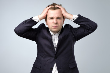 Doubtful handsome man in suit standing touching his head and looking at caemra, thinking.