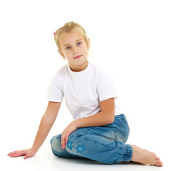 A little girl is sitting on the floor in a clean white T-shirt.