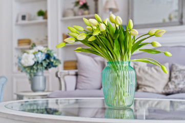 Vase with yellow tulips on the table in the room. Stylish interior background.