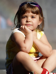 Little girl sitting watching others, summer weather, neutral background