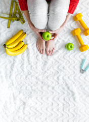 Girl on bed background top view with healthy food for diet and bars, measuring tape, wrist builder