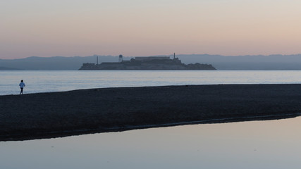 Obraz premium Lone jogger on the beach in San Francisco. Alcatraz Island outlined against early morning sky.