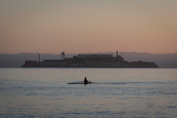 Solo rower in racing shell on calm water in front of Alcatraz.  