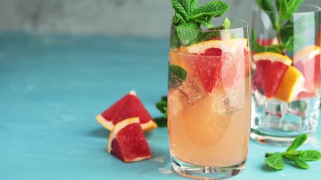 Grapefruit and fresh mint cocktail with juice, cold summer citrus refreshing drink gin tonic cocktail or beverage with ice on blue concrete surface. 59.95 fps