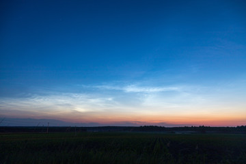 sunset over green field with noctilucent clouds