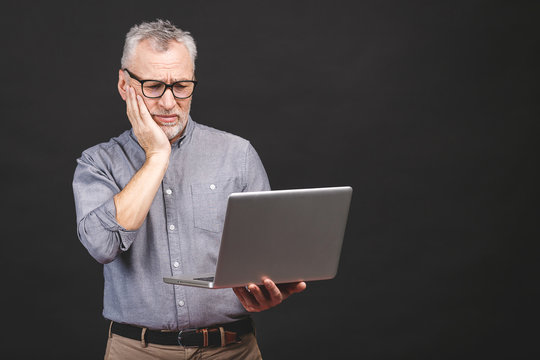 Too much work to do. Tired angry senior aged man with laptop computer isolated against black background.