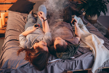 man and girl smoking in bed electronic cigarettes vape-mod and drip. Couple vaping.