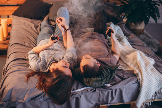 Man And Girl Smoking In Bed Electronic Cigarettes Vape-mod And Drip. Couple Vaping.