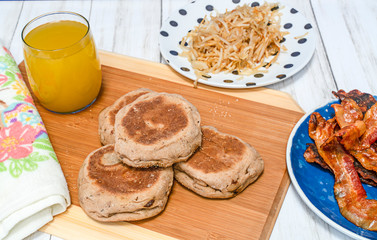 Breakfast of bacon, hash brown potato, muffin and juice.