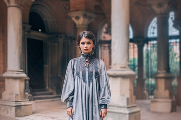terrible cold look of nun makes them afraid, a girl with dark hair gathered looks at camera, lady in long, free, simple gray velor dress, old columns like in museums, creative colors and soft light